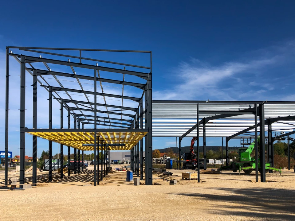 Main courbe sur un chantier de construction moderne dessinant au crayon rouge les plans d'une extension contemporaine à structure métallique et baies vitrées