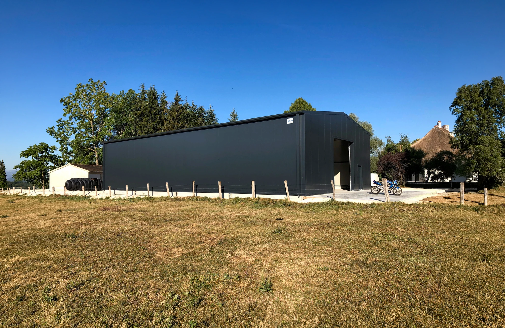 Vue aérienne d'un hangar agricole ouvert, structure métallique avec toiture en tôle ondulée rouge, éclairage zénithal par lanterneaux translucides