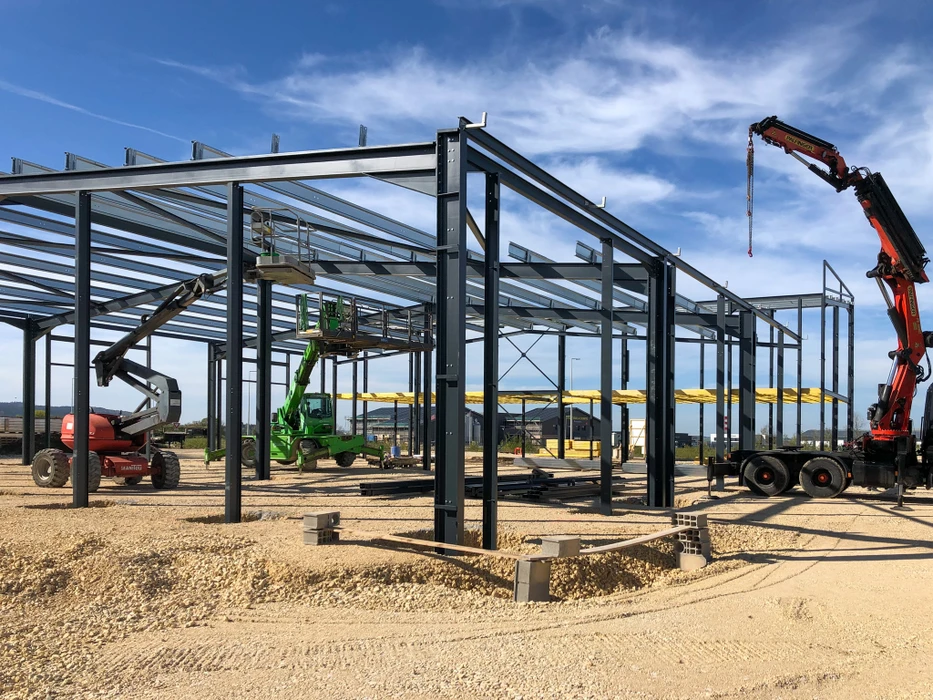 Chantier de construction en extérieur avec ouvriers en silhouette travaillant sur échafaudage métallique modulaire contre ciel bleu