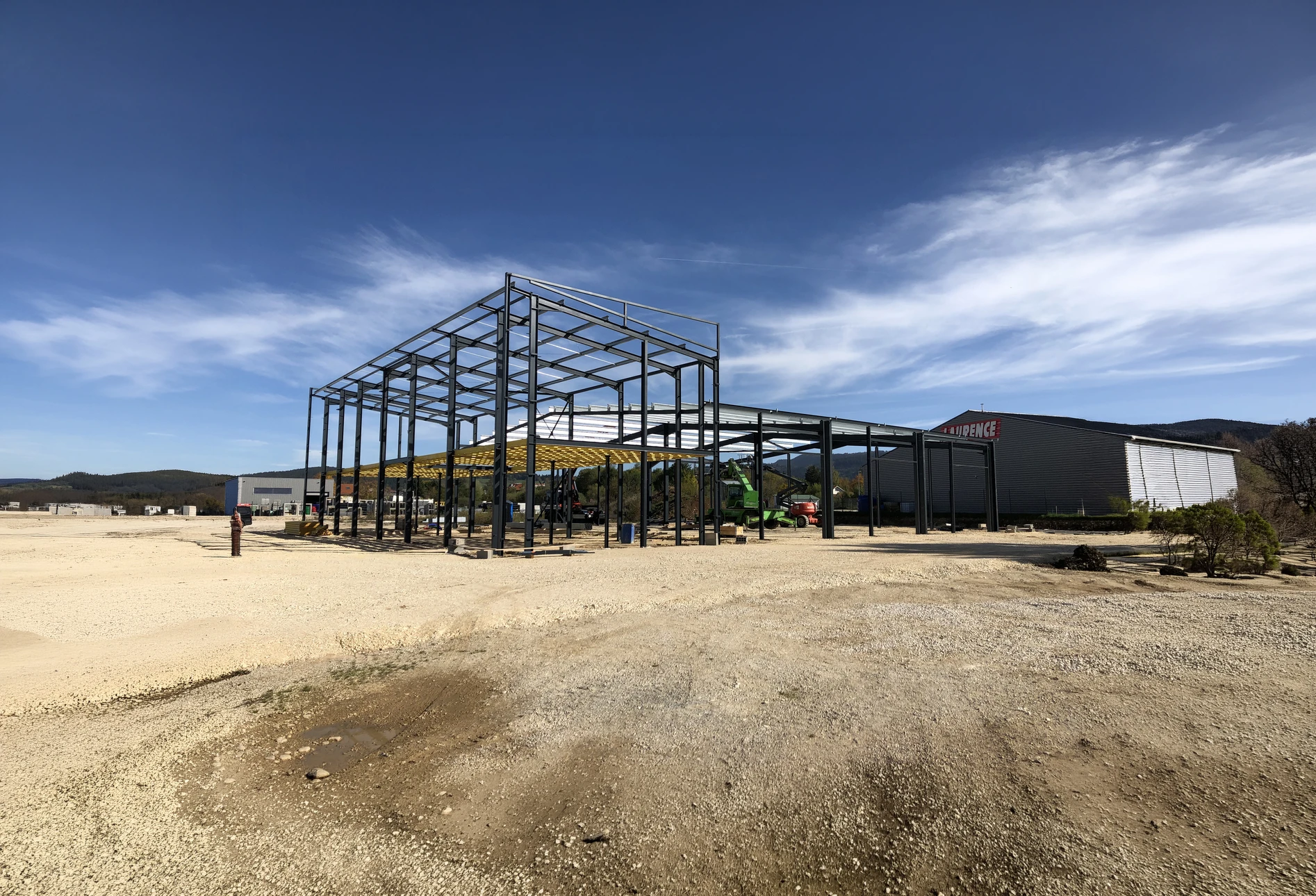 Vue aérienne d'un hangar agricole ouvert, structure métallique avec toiture en tôle ondulée rouge, éclairage zénithal par lanterneaux translucides