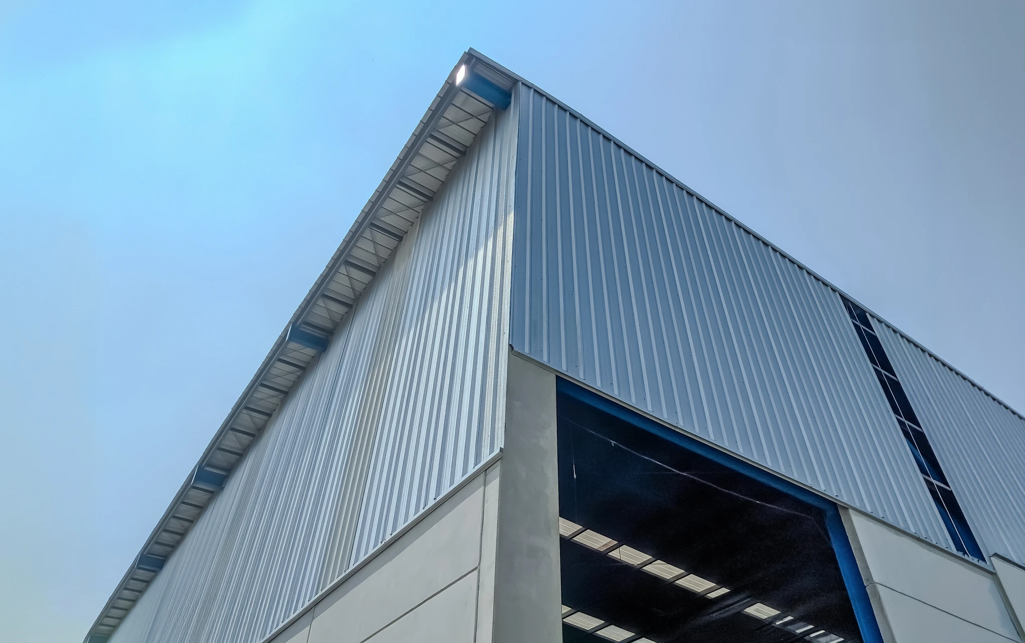 Vue aérienne d'un hangar agricole ouvert, structure métallique avec toiture en tôle ondulée rouge, éclairage zénithal par lanterneaux translucides